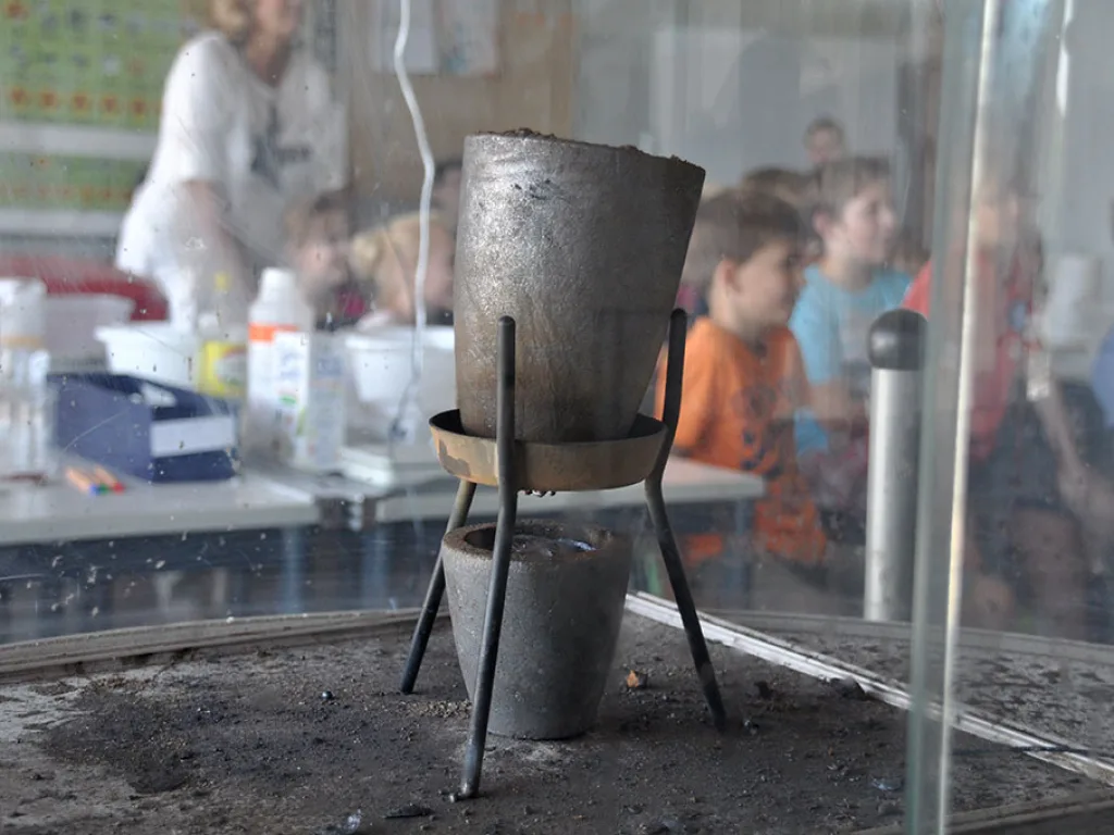 Ein Metalltrichter steht auf einem Stativ, dahinter beobachten Kinder.
